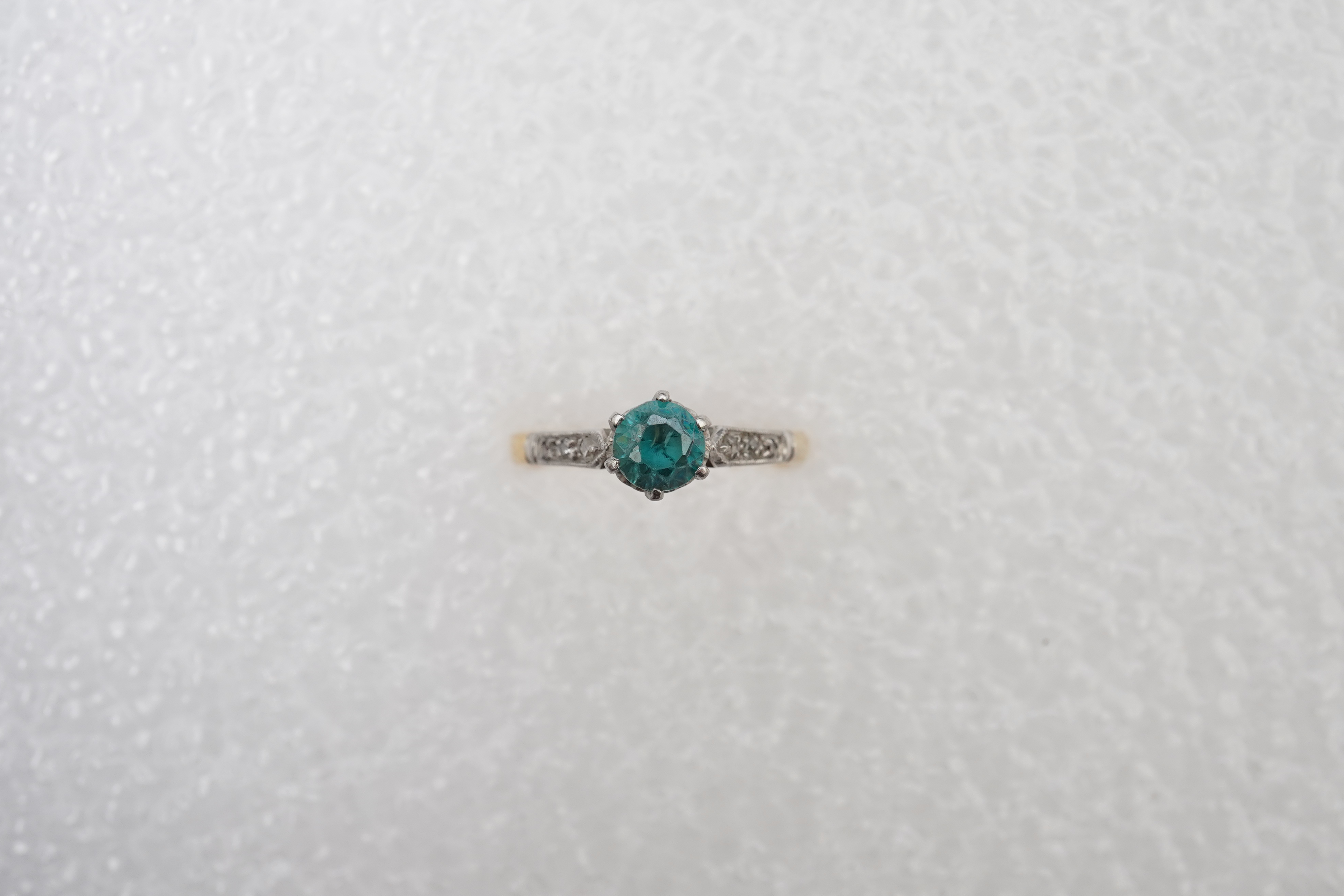 A zircon and diamond ring, mid 20th century, claw-set with a brilliant-cut blue zircon measuring approximately 5mm diameter, to shoulders set with rose-cut diamonds, mounted in gold, size N, stamped 18CT, gross weight ap